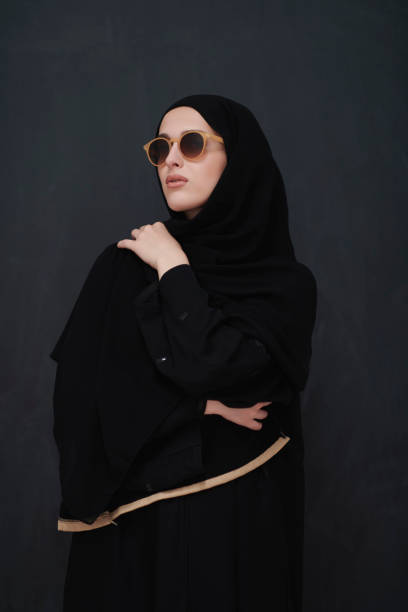 Young muslim in traditional clothes or abaya and sunglasses posing in front of black chalkboard Young muslim in traditional clothes or abaya and sunglasses posing in front of black chalkboard. Arab woman representing modern arabic lifestyle, islamic fashion and Ramadan kareem concept arabian sunglasses stock pictures, royalty-free photos & images