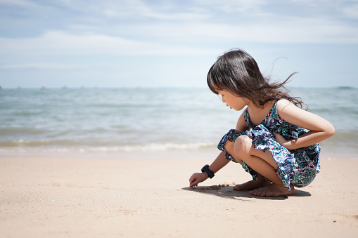 Asian happy little girl is sitting playing the beach by the sea having fun on summer vacation weekend