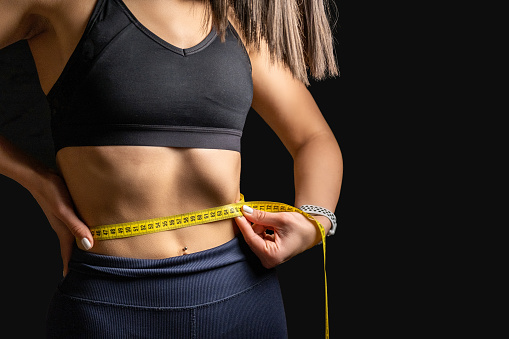 Athlete young woman is measuring her waist with a tape measure.