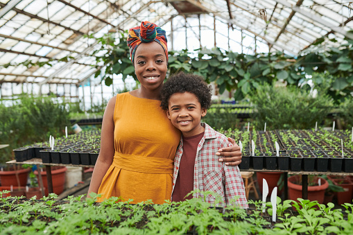 Portrait of happy woman embracing the boy and smiling at camera while standing in greenhouse