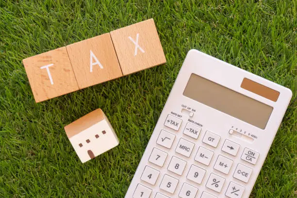 TAX; Three wooden blocks with "TAX" text of concept, a house toy, and a calculator.