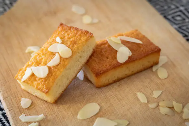 Close-up of a partially eaten financier cake on a cutting board sprinkled with flaked almonds