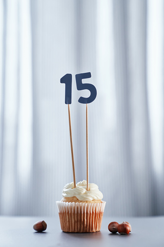 Homemade tasty cupcake or muffin with number 15 fifteen and hazelnuts on table and bright background. Birthday or anniversary greeting card concept. High quality vertical photo