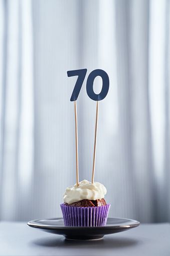 Anniversary digital greeting card concept. Tasty chocolate birthday cupcake or muffin with number 70 seventy on black plate with bright background. High quality vertical photo