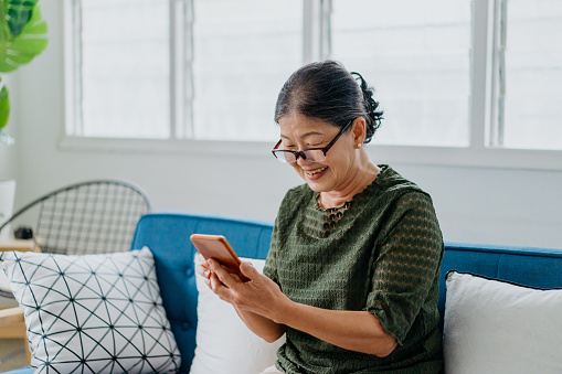 Image of a smile senior Asian Chinese woman using smartphone at home