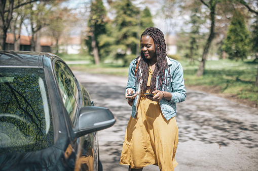 Smiling african woman standing next to car on road and unlocking door