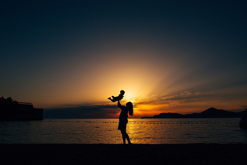 Mom throws up her little son and plays with him on the beach at sunset . High quality photo