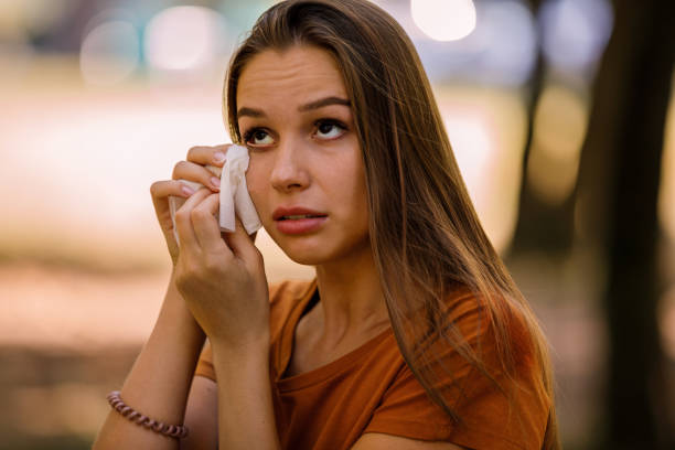 Young Woman is Having Allergy Problems Outside in Nature and Rubbing her Eyes. A Woman of Caucasian Ethnicity with Long Hairis Rubbing her Eyes with Paper Handkerchief Due to Problems with Sight in the Public Park. wiping tears stock pictures, royalty-free photos & images