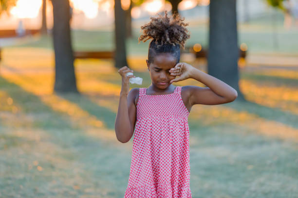 Cute African-American Girl is Having an Allergy Outside and Rubbing her Eyes. Young African Girl is Walking in the Park But Feeling Uncomfortable Due to the Problems with her Eyes, so She is Rubbing them. human eye scratching allergy rubbing stock pictures, royalty-free photos & images