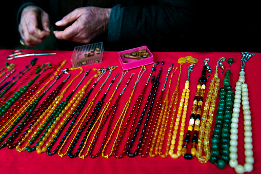 There are colorful rosaries on the pink background. They are organized for sale. The seller's hands are also visible in the frame in Turkey.