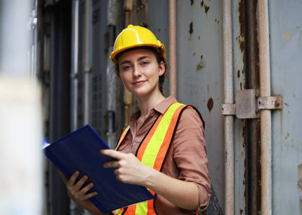 Young woman engineers standing in the shipping yard tracking the cargo inventory and checking container box for safety. stock photo