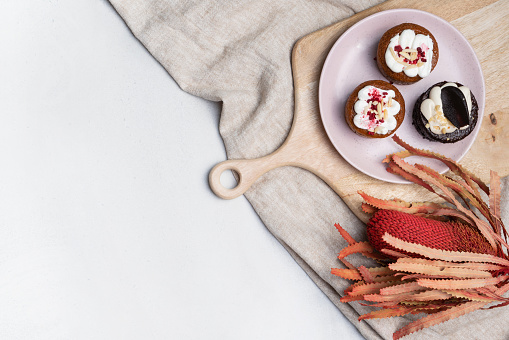 A plate of assorted vegan cup cakes or raw dessert, decorated by an Australian native dried red Banksia, on a neutral background. For Valentines day, Easter, Anniversary or Mothers day events.