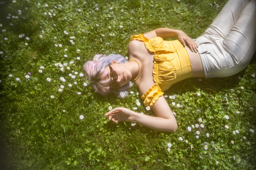 Young girl with colored hair lies on the daisy blooming grass