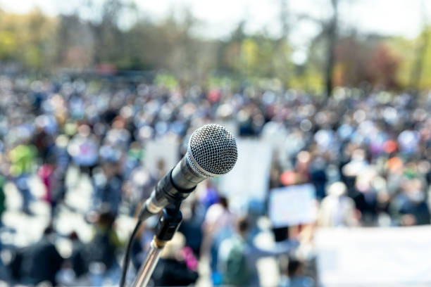 protesta o manifestazione pubblica, focus sul microfono, gruppo sfocato di persone in sottofondo - protest foto e immagini stock