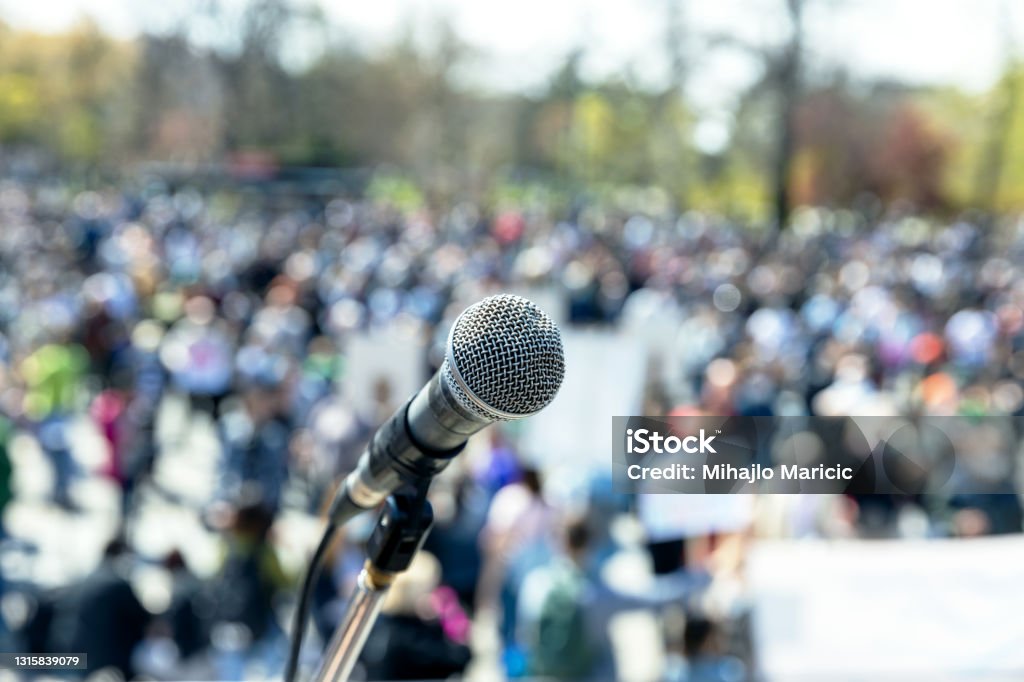 Protest or public demonstration, focus on microphone, blurred group of people in the background Protest or public demonstration, focus on microphone, blurred crowd of people in the background Protest Stock Photo