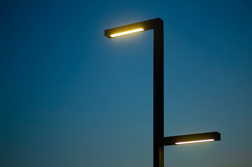 Lamp post against the background of the night sky. Modern lamppost with evening electric lighting. Minimal art photography.