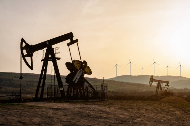 pompe per olio e mulini a vento elettrici al tramonto - pompa di estrazione petrolifera foto e immagini stock