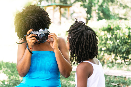 unrecognizable African American adult woman holding an analog camera making a selfie to a little boy.