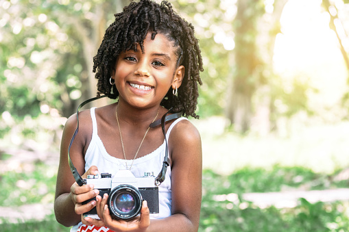 portrait of a young african american toddler girl holding an old camera and looking at camera.