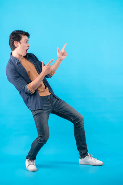 istock Cheerful Asian male man indicate thumb empty space hand gesture finger point wide smile open mouth wear casual cloth jeans isolated blue color background 1315852730