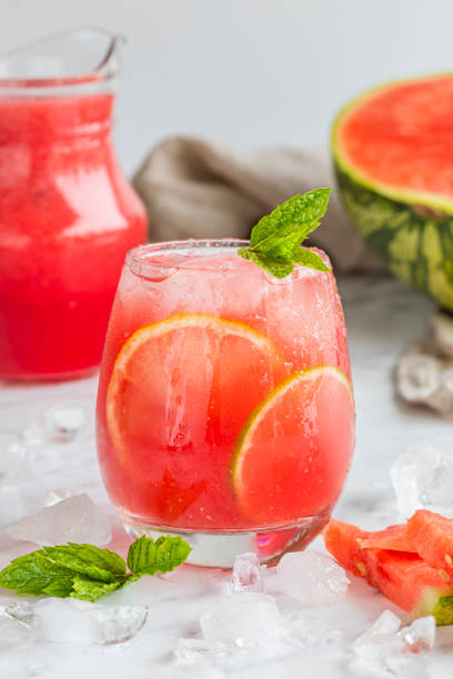 A watermelon drink watermelon, lemon, lime, mint and ice Watermelon mojito fresh red drink. With watermelon, lemon, lime, mint leaves and ice. The drink is on a white table with a half watermelon in the background and ice and mint scattered on the table. punch drink stock pictures, royalty-free photos & images