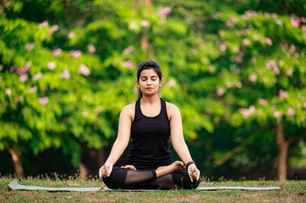 Young woman meditating outdoors at park Young Asian/ Indian woman wearing black sports dress and meditating outdoors at park. yoga stock pictures, royalty-free photos & images