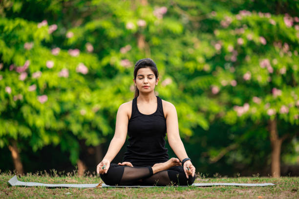 Young woman meditating outdoors at park Young Asian/ Indian woman wearing black sports dress and meditating outdoors at park. yoga lotus position meditating women stock pictures, royalty-free photos & images