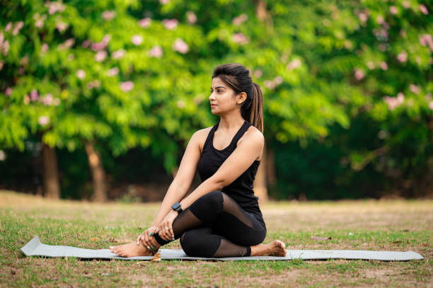 istock Young woman sitting on exercise mat and performing yoga at park 1315856462