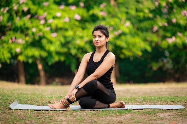 istock Young woman sitting on exercise mat and performing yoga at park 1315856464