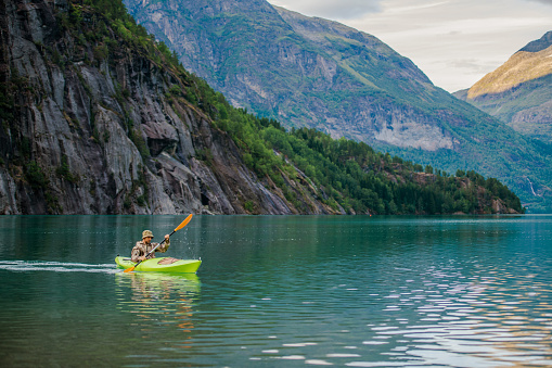 Caucasian Men in a Kayak on Glacial Lake in the Norway Exploring Fascinating Norwegian Nature From the Water. Recreation Theme.
