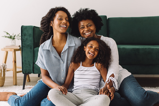 Cheerful woman with her two daughters at home. Mature woman sitting in living room with her daughters looking at camera and smiling.