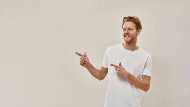 istock Young redhead guy smiles and points with fingers on the left side 1315870641