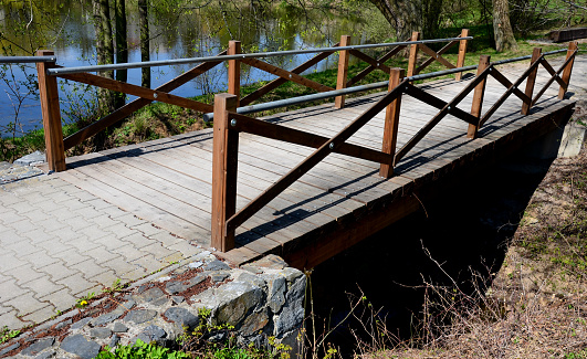 wooden bridge with a stone foundation newly built for cyclists over a stream by the pond. wooden beams connected by screws and metal railings