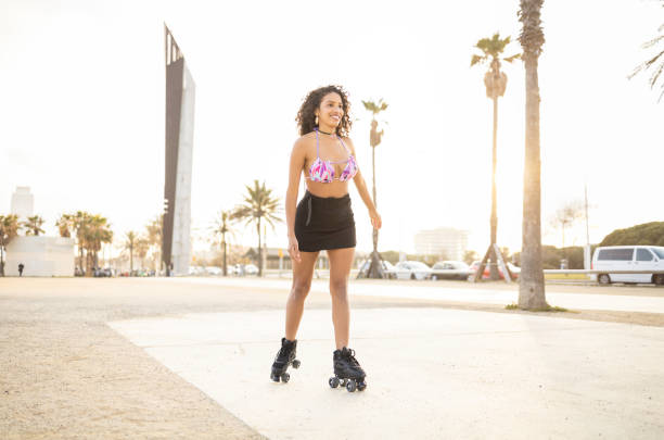 Young fit black woman on roller skates riding outdoors on urban street. Smiling girl with afro hairstyle rollerblading on sunny day