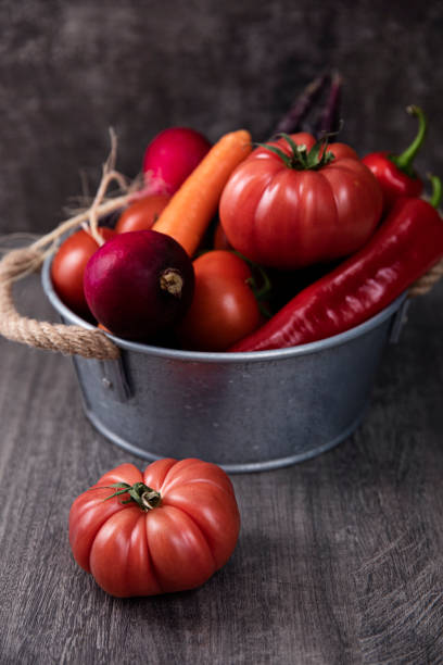 Fresh tomatoes, red peppers, carrots, and radish in a basket on dark wooden background