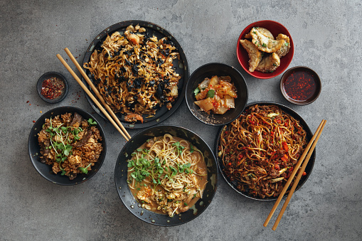 Spicy Korean beef noodles (Shin Ramyun). Noodle with seafood such as shrimp, squid, baby octopus and crab are braised in spicy seasoning with various vegetables (Haemul Jjim). Chicken noodle soup (Dak Kalguksu). Beef fried rice. Asian pickles. Flat lay top-down composition on concrete background.