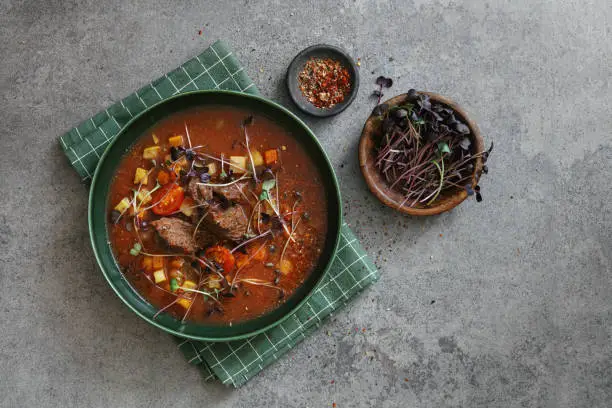 Beef-cheek minestrone with tomato, carrot, celery and zucchini. Flat lay top-down composition on concrete background.