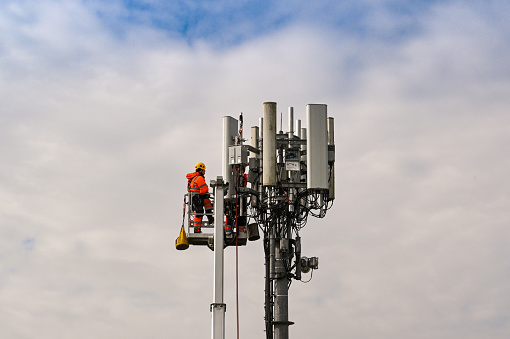 Pencoed, near Bridgend, Wales - April 2021: Engineer in a hydraulic platform at the top of a mobile phone transmitter mast for maintenance work
