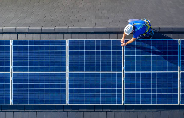 Solar panel installer installing solar panels on roof of modern house Male engineer in blue suit and protective helmet installing photovoltaic panel system. Professional electrician mounting solar module on roof. Alternative energy ecological concept solar energy stock pictures, royalty-free photos & images