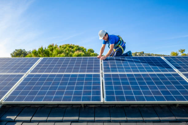 Solar panel installer installing solar panels on roof of modern house Male engineer in blue suit and protective helmet installing photovoltaic panel system. Professional electrician mounting solar module on roof. Alternative energy ecological concept Solar Energy stock pictures, royalty-free photos & images