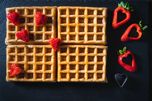 Waffles with strawberries with heart shape on moody dark background