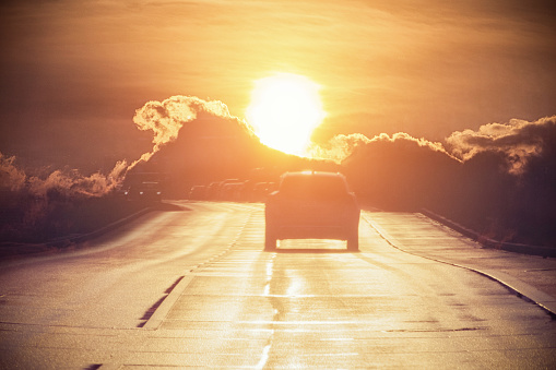 Car on the country road in the backlight of the setting sun