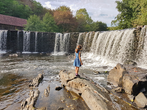 a girl near a waterfall by the river on rocks in nature in Limousin