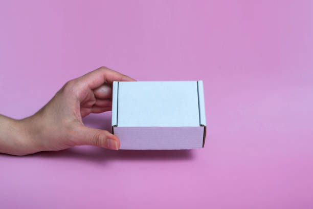 white corton box for mock-up in a female hand on a pink background. space for text