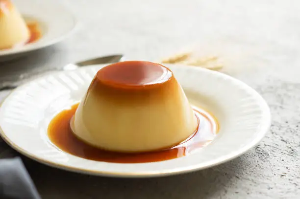 Cream caramel pudding with caramel sauce in plate on white rustic table