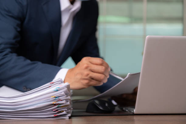 オフィスデスクに文書とコンピュータのラップトップを持ち、スーツを持ち、書いている男性のオフィスワーカー、ビジネス過負荷紙のスタック。 - stack paper document heap ストックフォトと画像