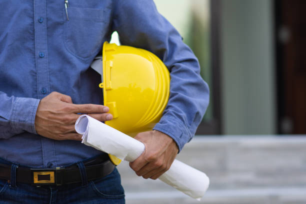 Contractor holding yellow helmet on site building construction , Engineer hold hard hat Engineer holding blueprint with yellow hard hat on site construction civil engineer stock pictures, royalty-free photos & images