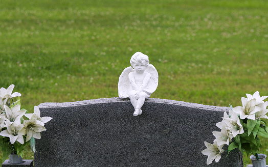 cherub statue carving on unmarked graveyard cemetery headstone marker with with flowers