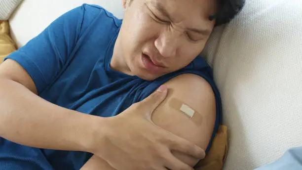 Close up young adult attractive hipster asia man receive covid-19 anti virus vaccine in campaign vaccination safe life got side effect pain at arm. Vaccine rollout swelling in volunteer.