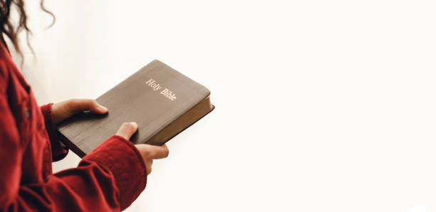 a young woman standing and praying on the bible, copy space. beside the mirrored window - bible holding reading book imagens e fotografias de stock